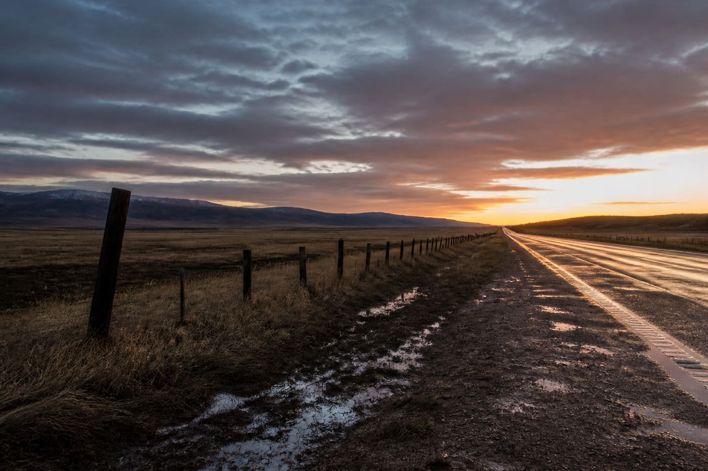 Wet gravel highway shoulder and fence line on the Wyoming plains